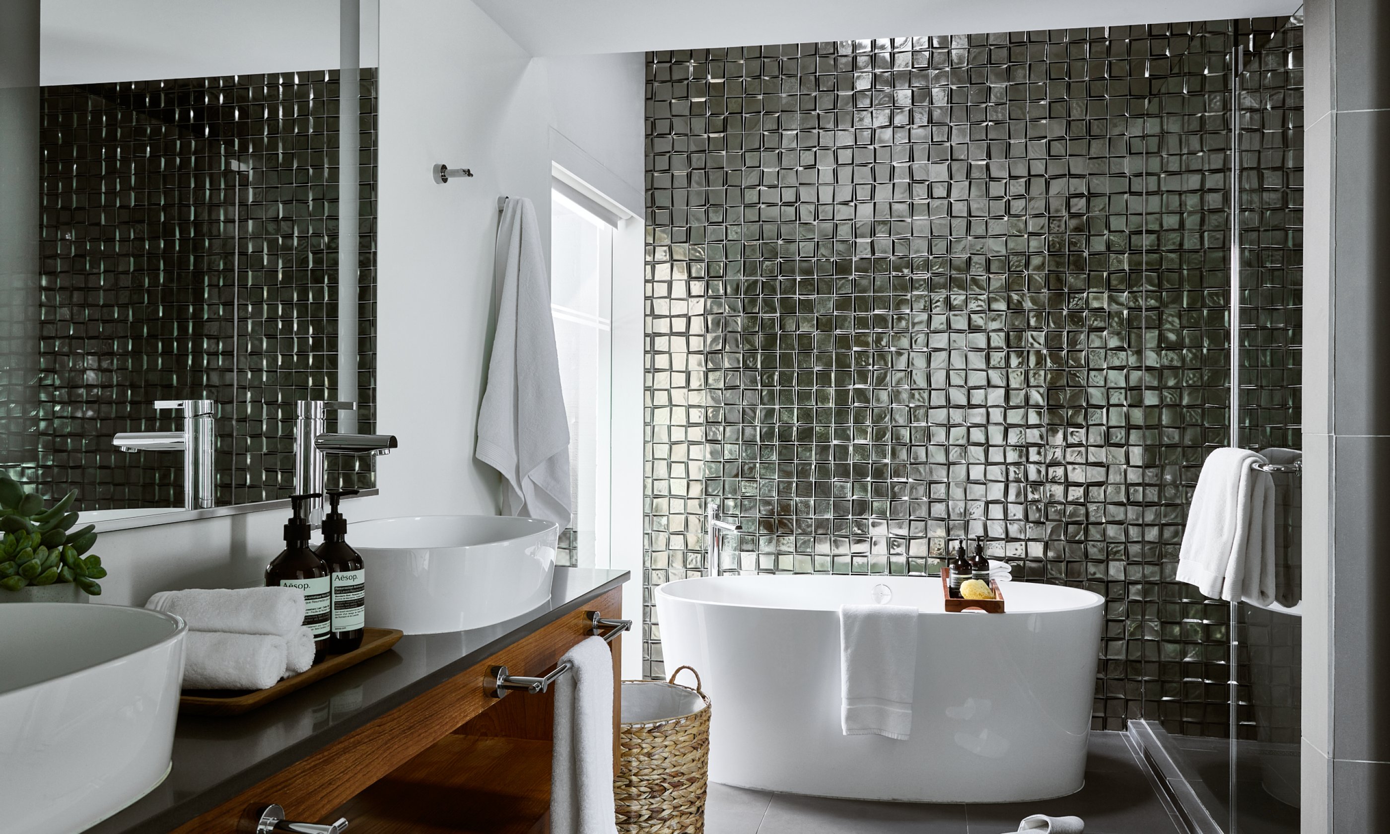 Metallic tiled bathroom with two sinks, vanity,  oversized soaking tub and walk-in shower.