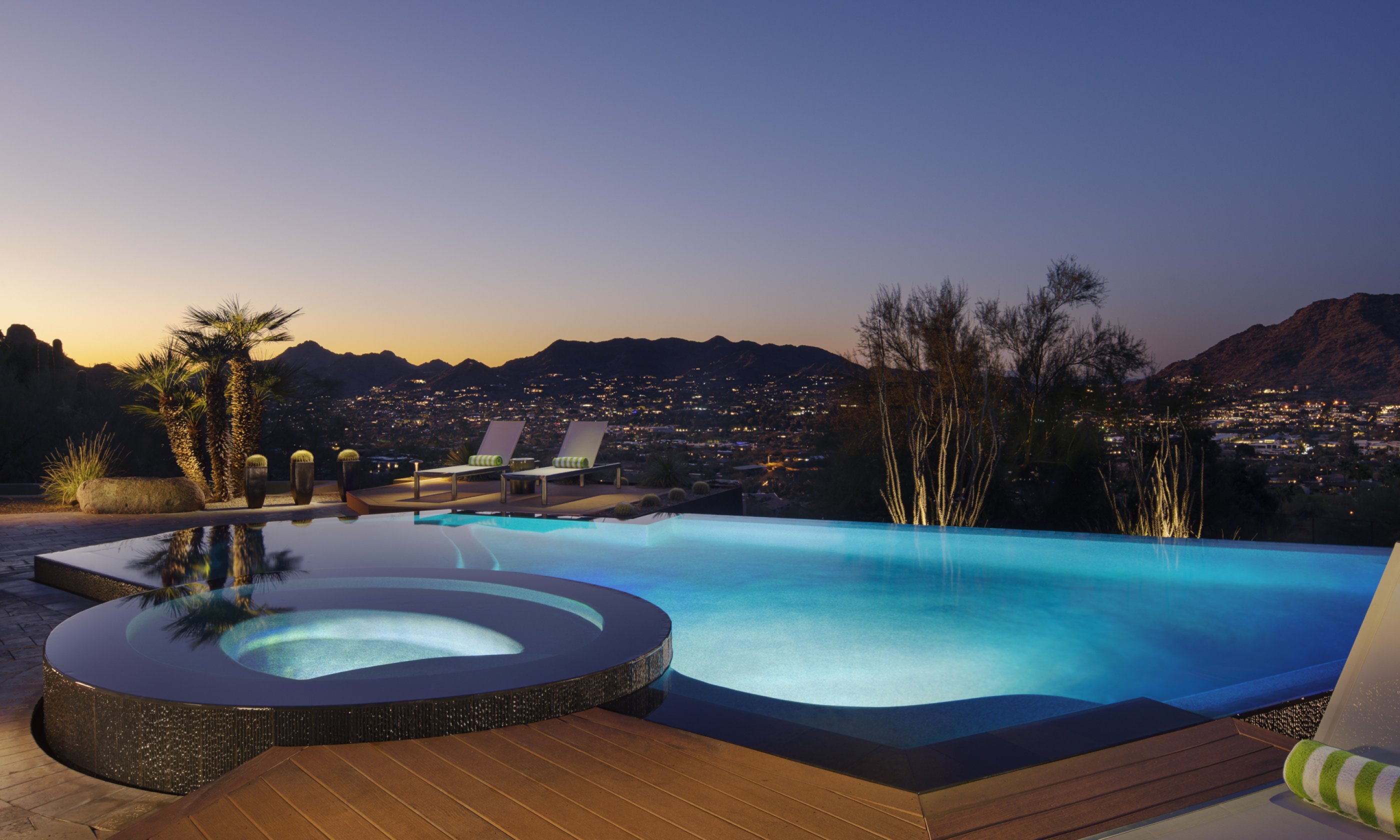 Hot tub and pool with two lounge chairs overlooking surrounding valley at dusk.