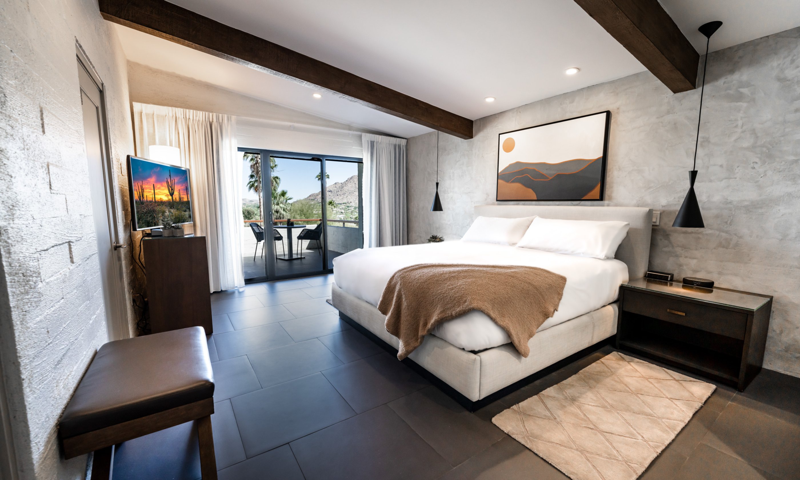 Suite bedroom with King bed, accent wall with art, nightstand with light, flatscreen television, dresser and wrap around patio.