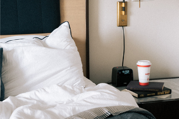 Messy bed with alarm clock and paper coffee cup on nightstand