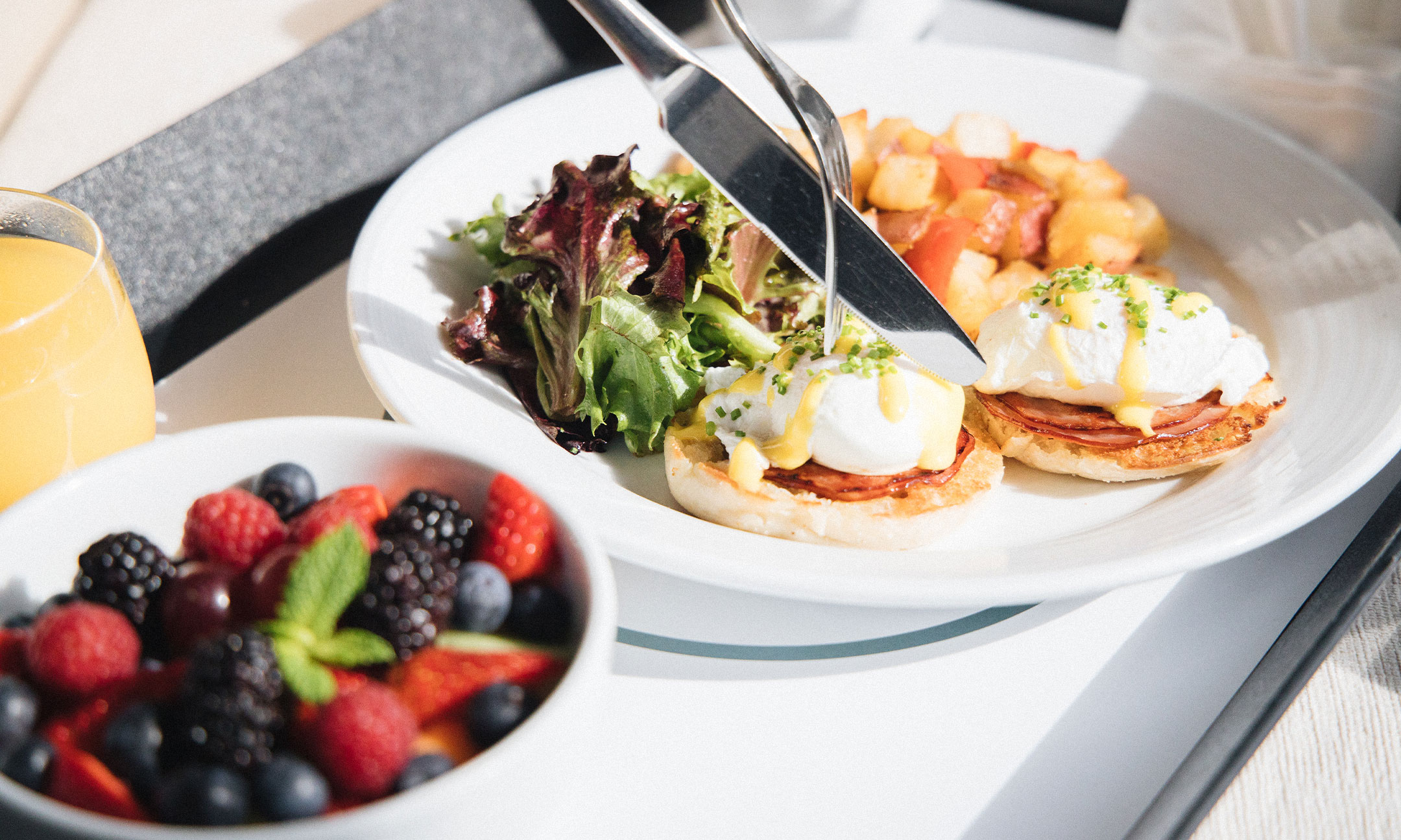 Eggs Benedict with a bowl of berries and a glass of orange juice