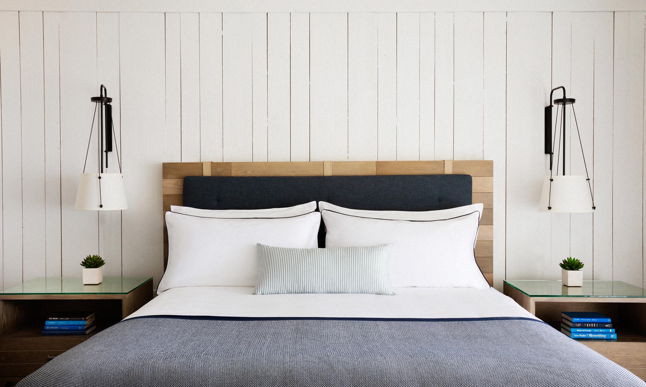 Bed with side tables and two hanging lamps with white plank wall