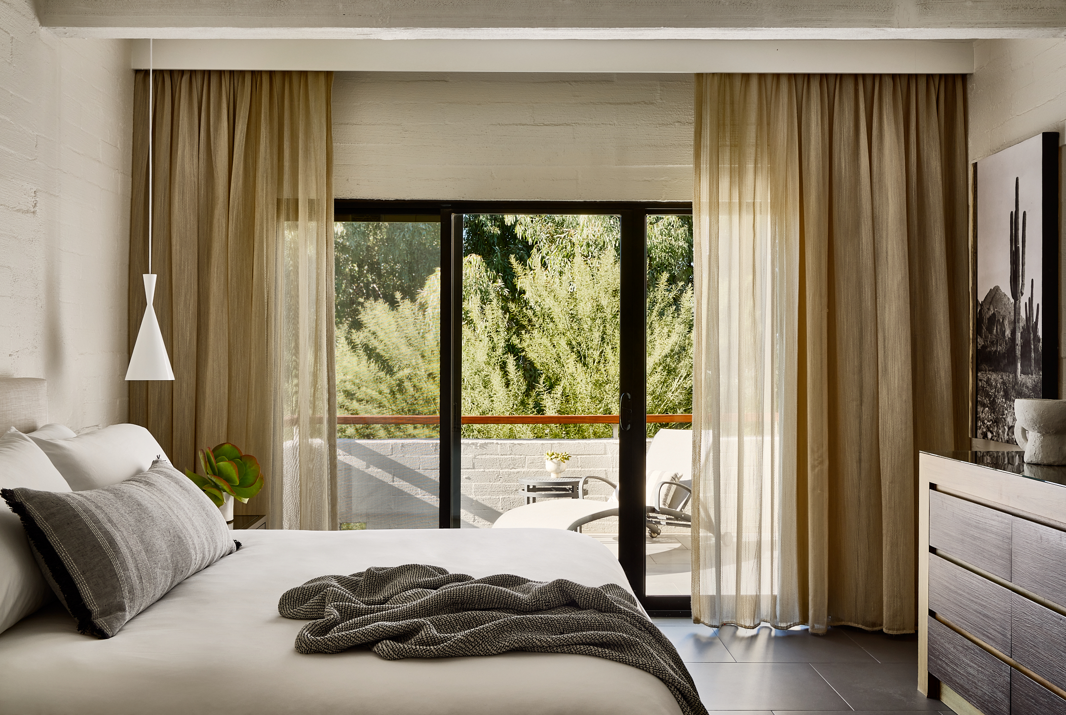 Bedroom with king bed, dresser and outdoor patio with lounge chair.