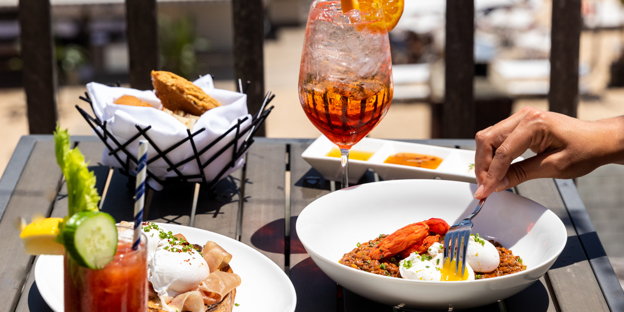 Hand with fork digging into brunch spread outdoor at Scarpetta Beach.