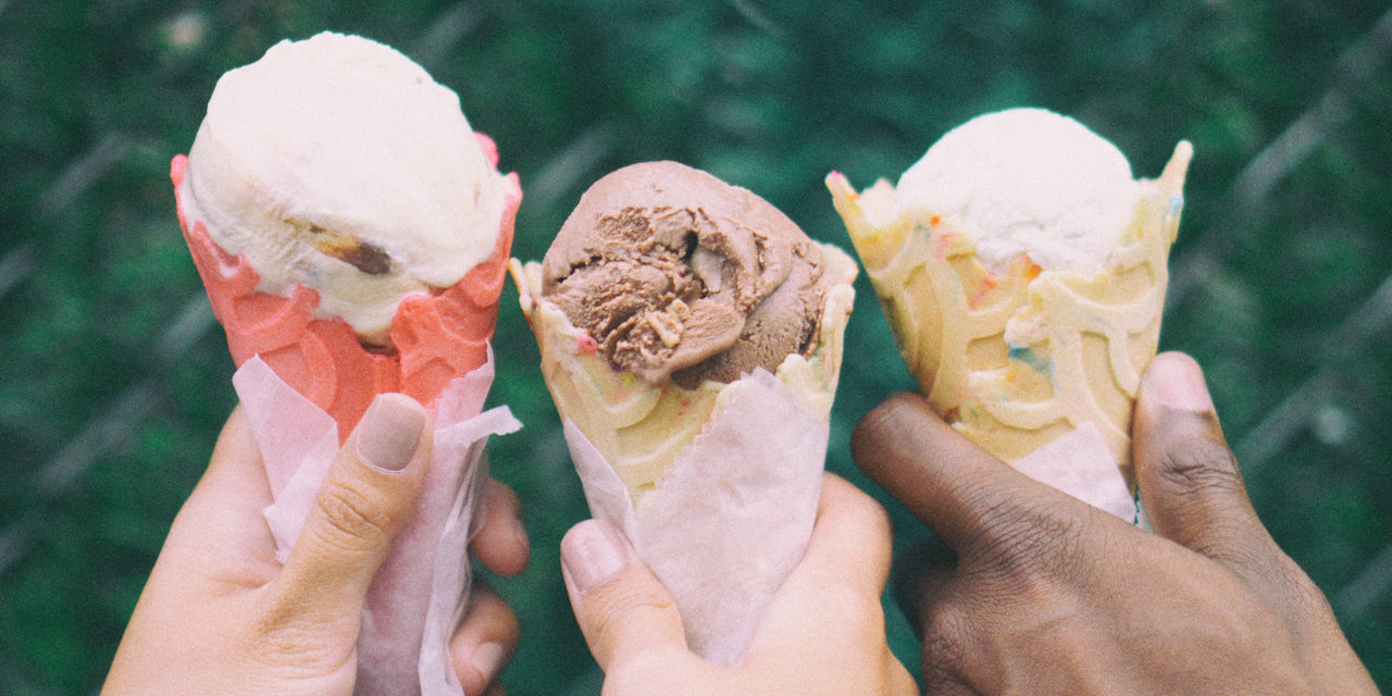 Three people's hands holding ice cream cones.