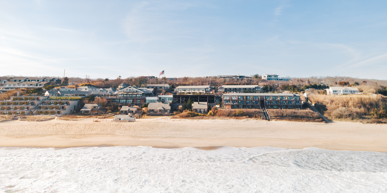 Drone shot of waves crashing on shoreline with Gurney's Montauk during fall.