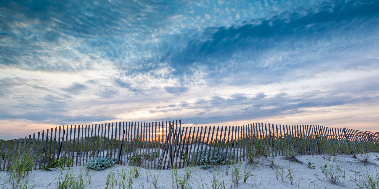 Beach wooden fence with colorful Montauk sunset in background.