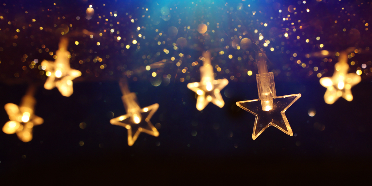 Glowing gold stars with lights inside hanging in front of blue background.