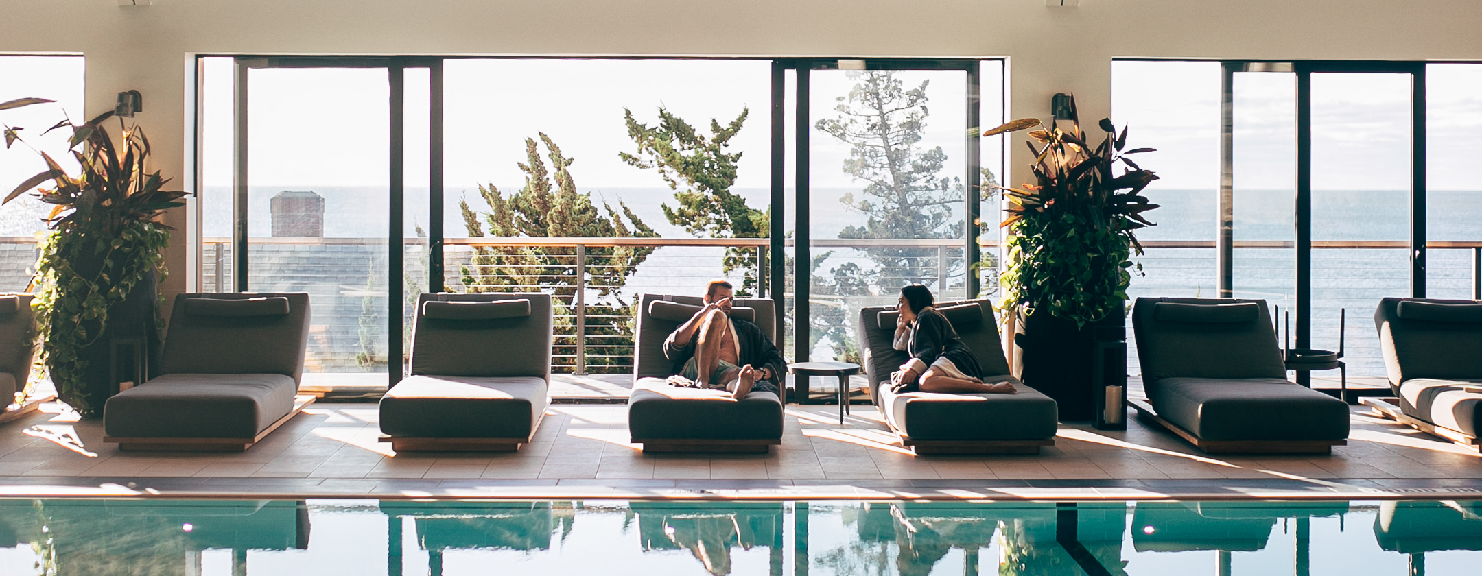 Couple in robes relaxing on lounge chairs beside Seawater Spa's indoor pool.