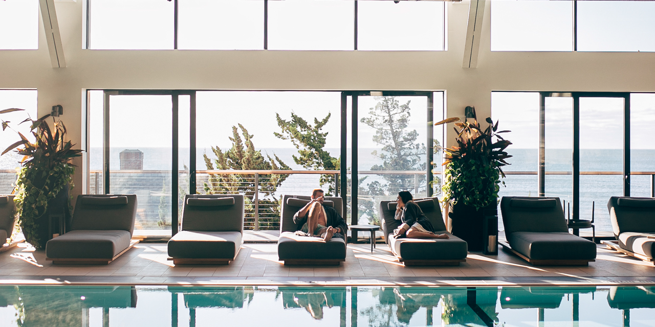 Couple in robes relaxing on lounge chairs beside Seawater Spa's indoor pool.