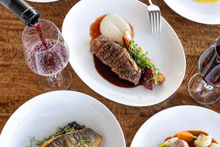 A waiter pours wine in a glass placed next to a plate of steak and other entrees at Scarpetta Beach restaurant.