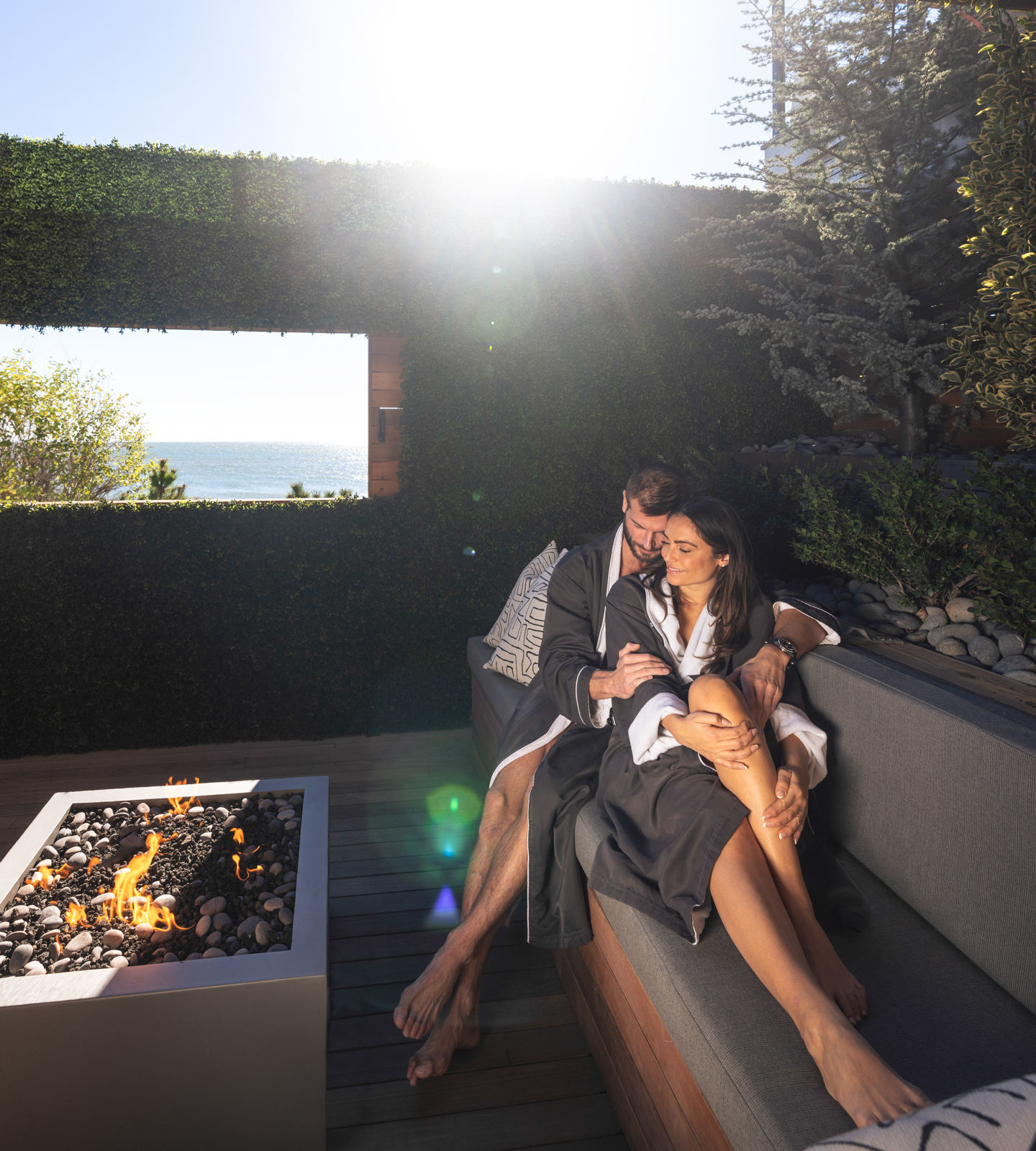 Couple in robes cuddling by outdoor fire pit in private treatment suite at Gurney's Seawater Spa.