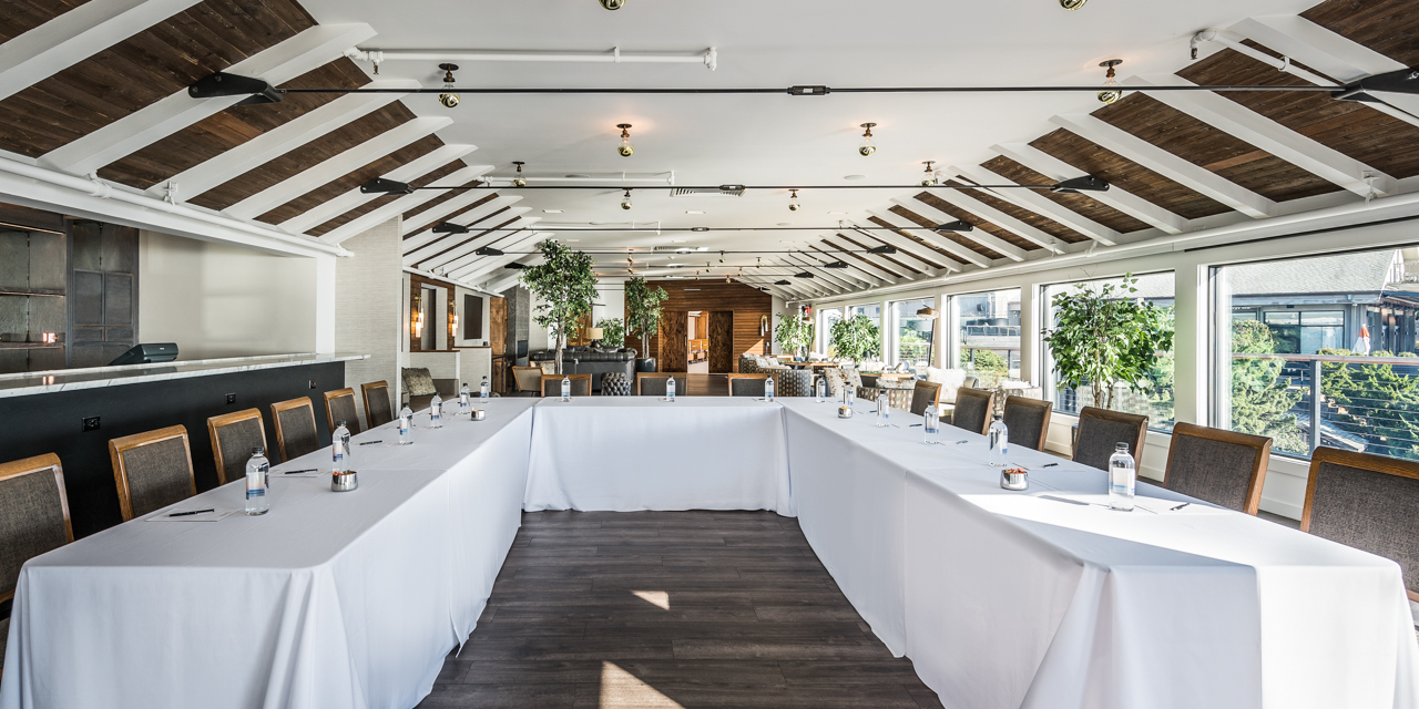 Regent Lounge with wood flooring, white walls and ceiling with wood panel accents, u-shaped table setup with white linen and wooden chairs.