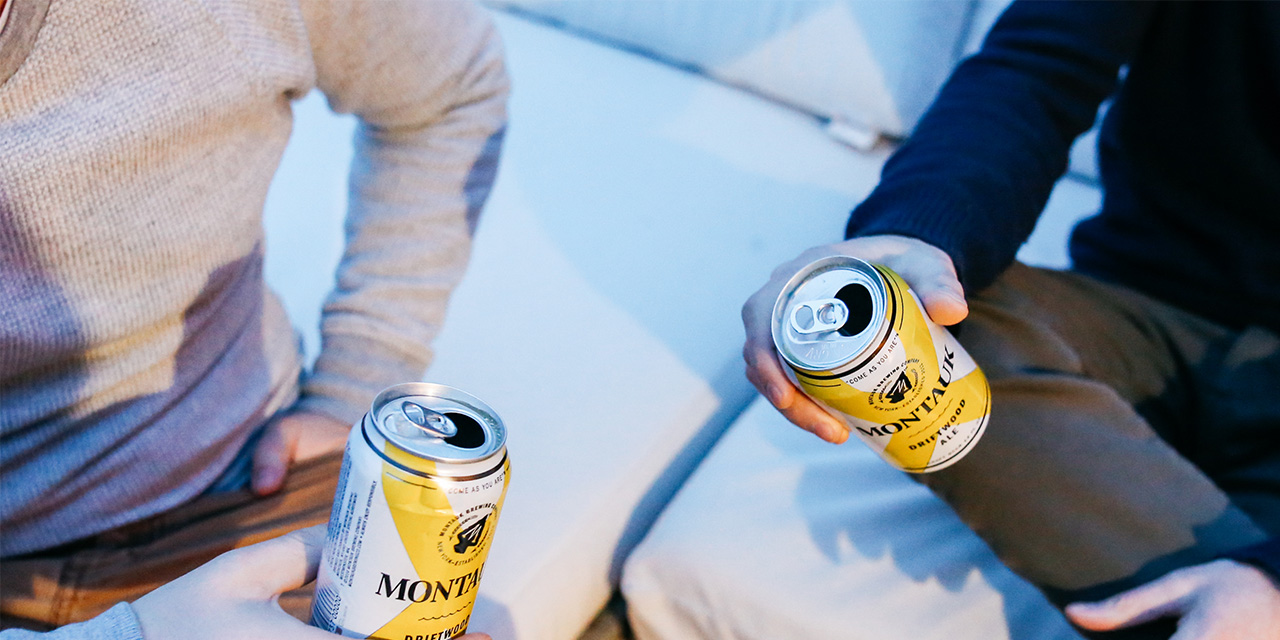 Two men seated facing one another while holding cans of beer at Gurney's Montauk Resort 