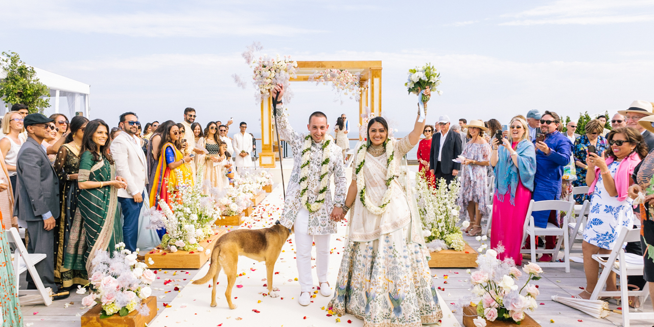 Bride and Groom with dog walking down the aisle celebrating as friends and family cheer after wedding ceremony.