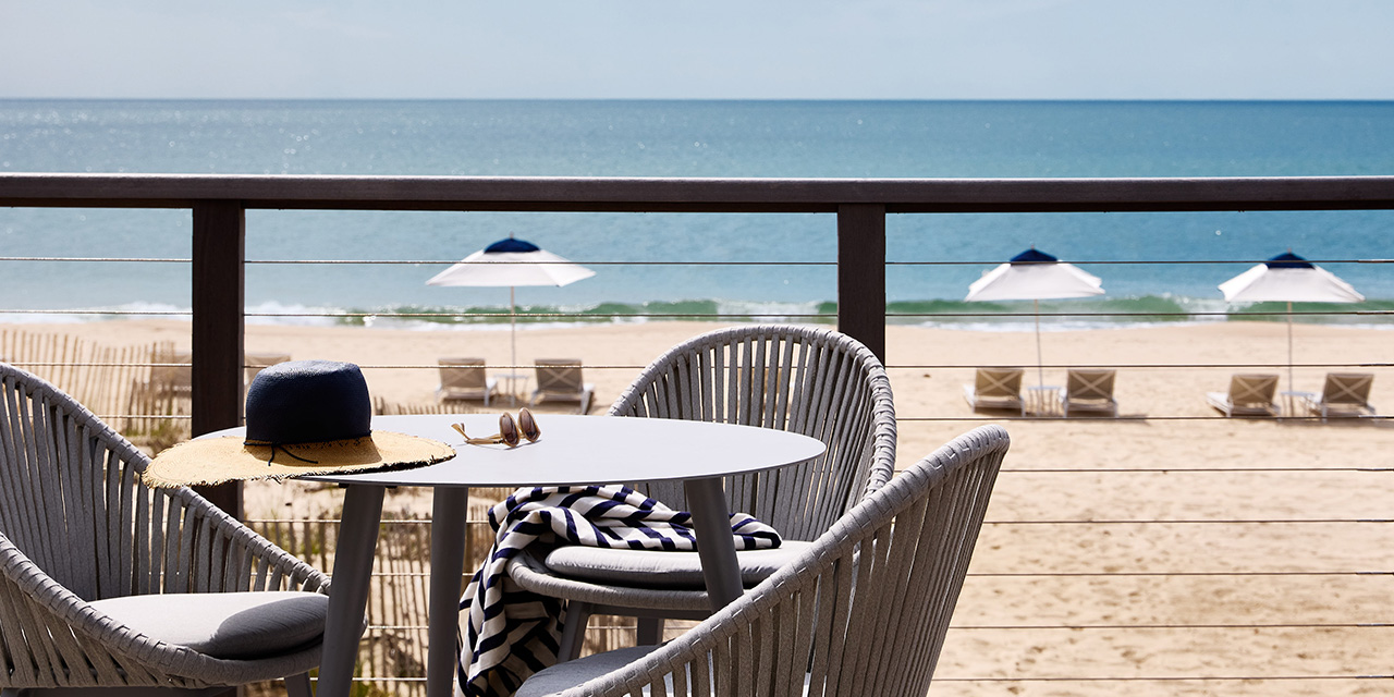 A hat and sunglasses on an outdoor dining table overlooking the ocean