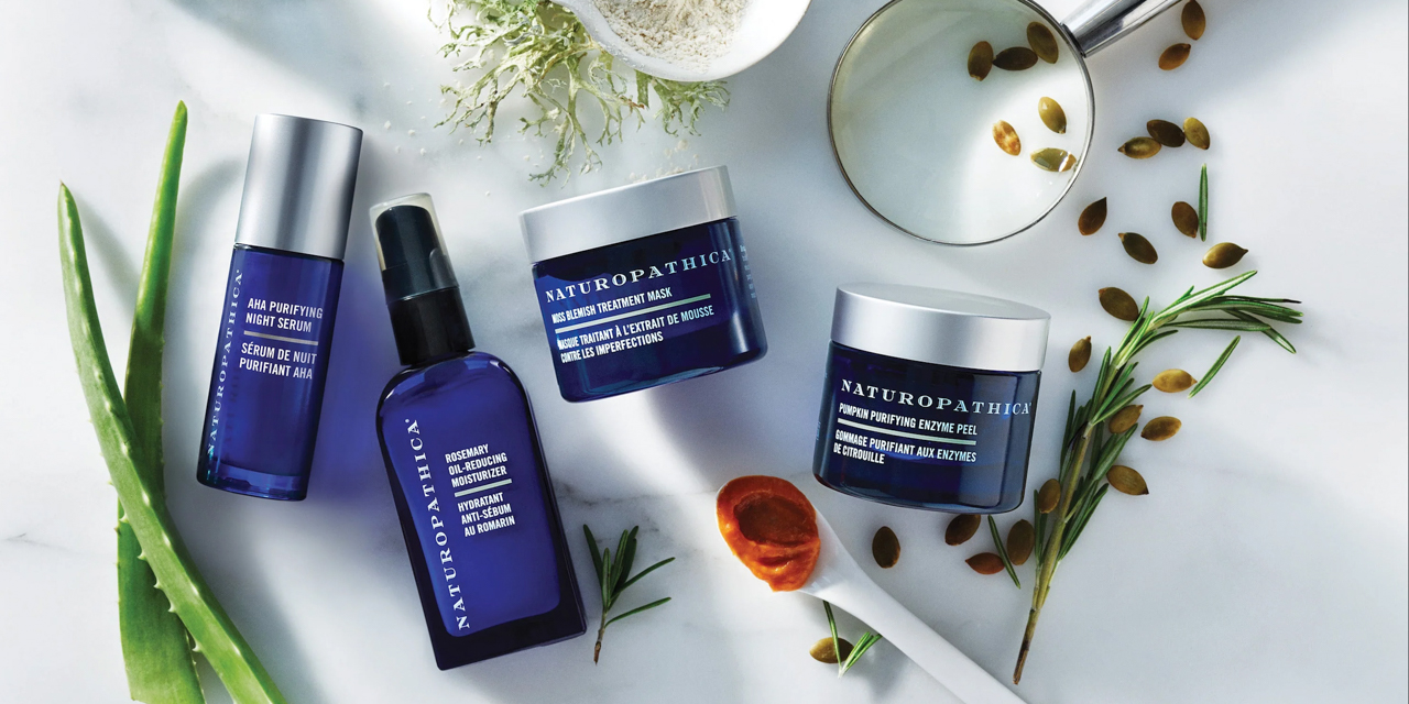 An array of Naturopathic skin products in blue packaging surrounded by fresh ingredients like aloe and collagen.