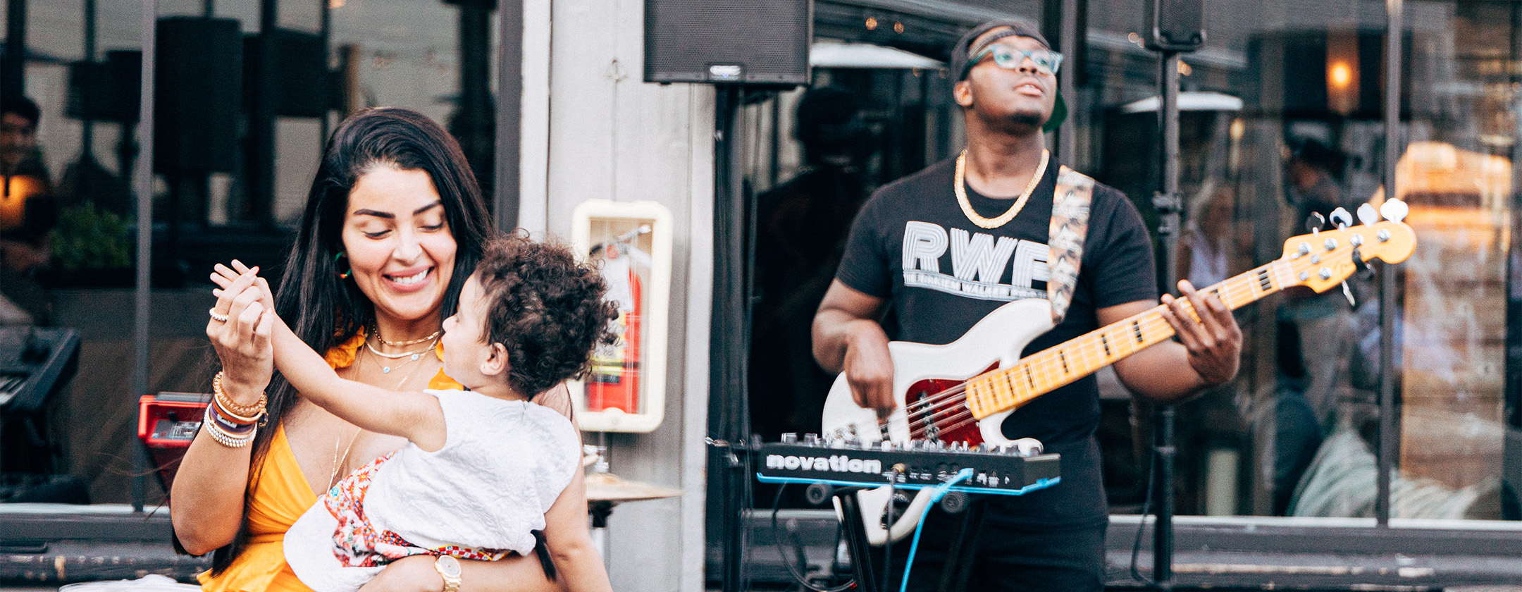 A woman dances with a small child in front of a man playing electric guitar.