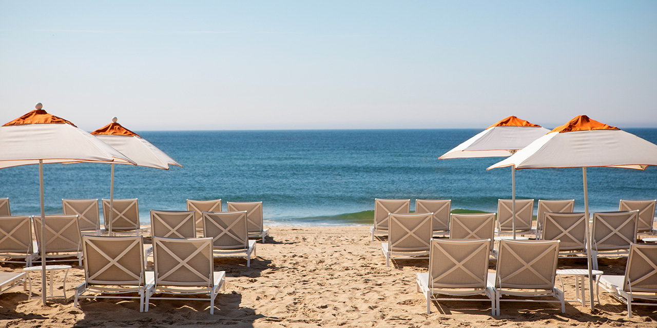 Rows of gray lounge chairs and white and orange umbrellas face the ocean at Gurney's Montauk beach club