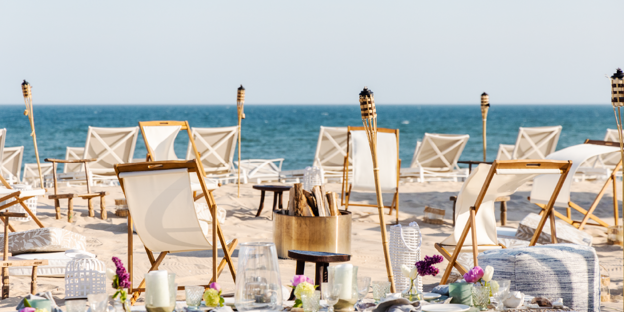 White canvas beach chairs circle a fire ring with a view of the ocean at Gurney's Montauk beach bonfires