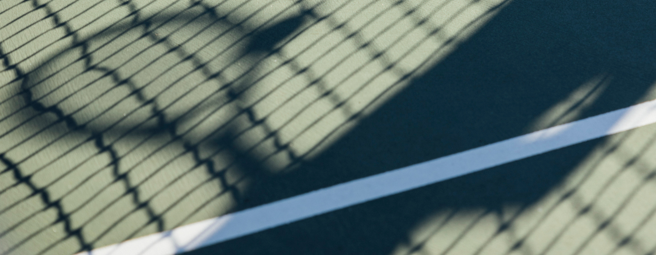 A close-up view of a tennis court with a net and shadows.