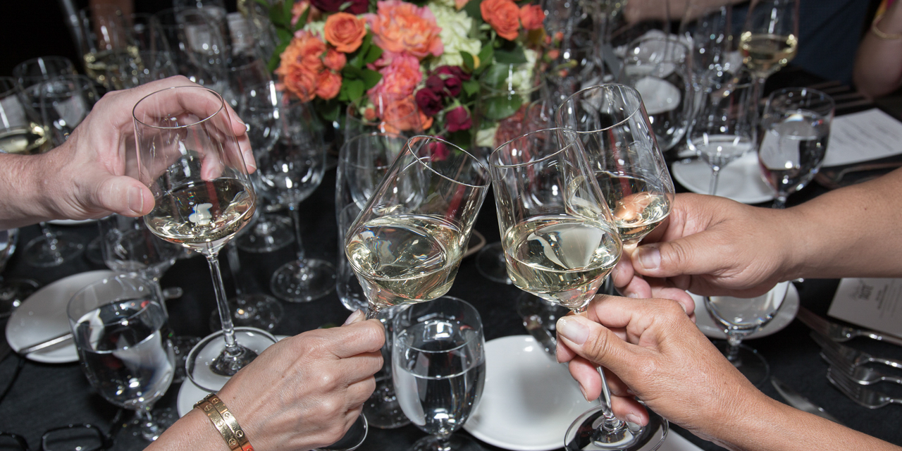 Group toasting with white wine at table with black table cloth and spring floral centerpiece.