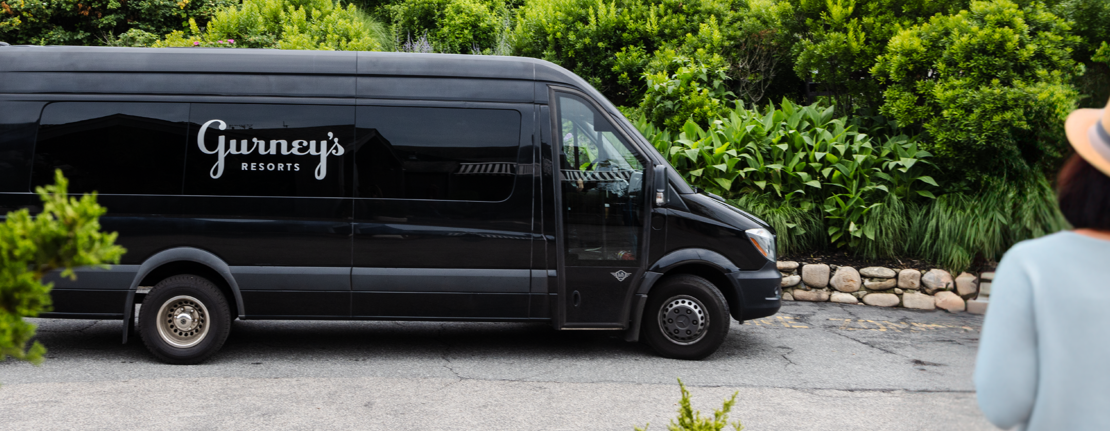 A black van with the words Gurney's Resorts on the side is parked in front of landscaping.