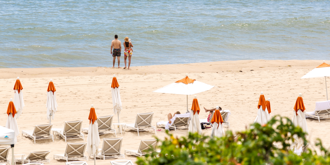 A couple with a small child stand near the water's edge on the private beach at Gurney's Montauk