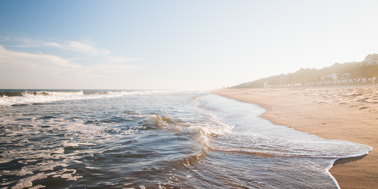 Waves crashing against shoreline in the afternoon with Gurney's Montauk in backdrop.