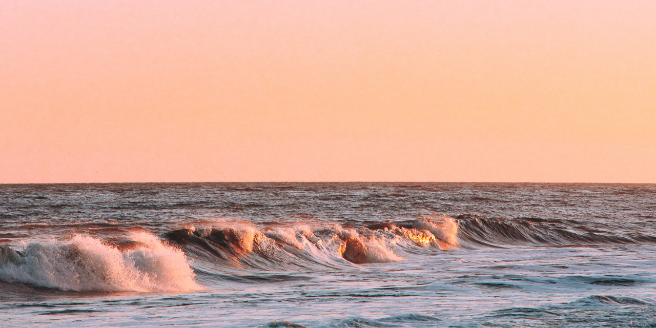 A pink sunset sets over rolling ocean waves at Gurney's Montauk Resort