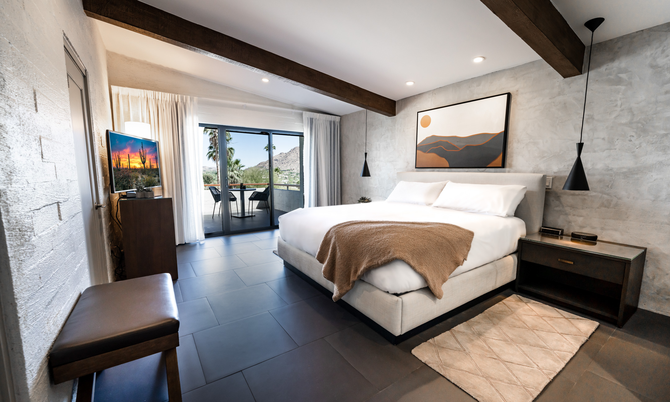 Suite bedroom with King bed, accent wall with art, nightstand with light, flatscreen television, dresser and wrap around patio.