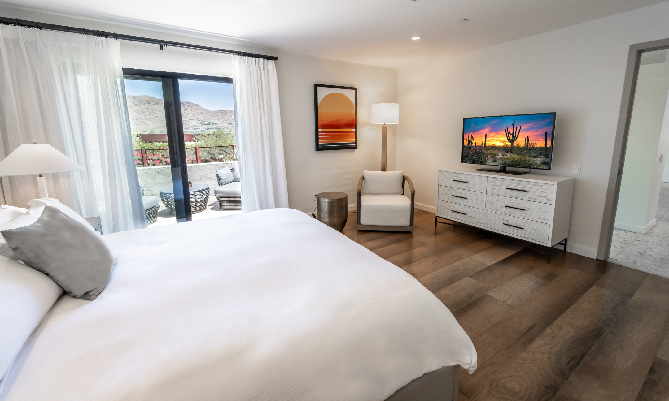 Guest bedroom with King bed, white dresser and chair, flatscreen television, wood flooring and outdoor patio.