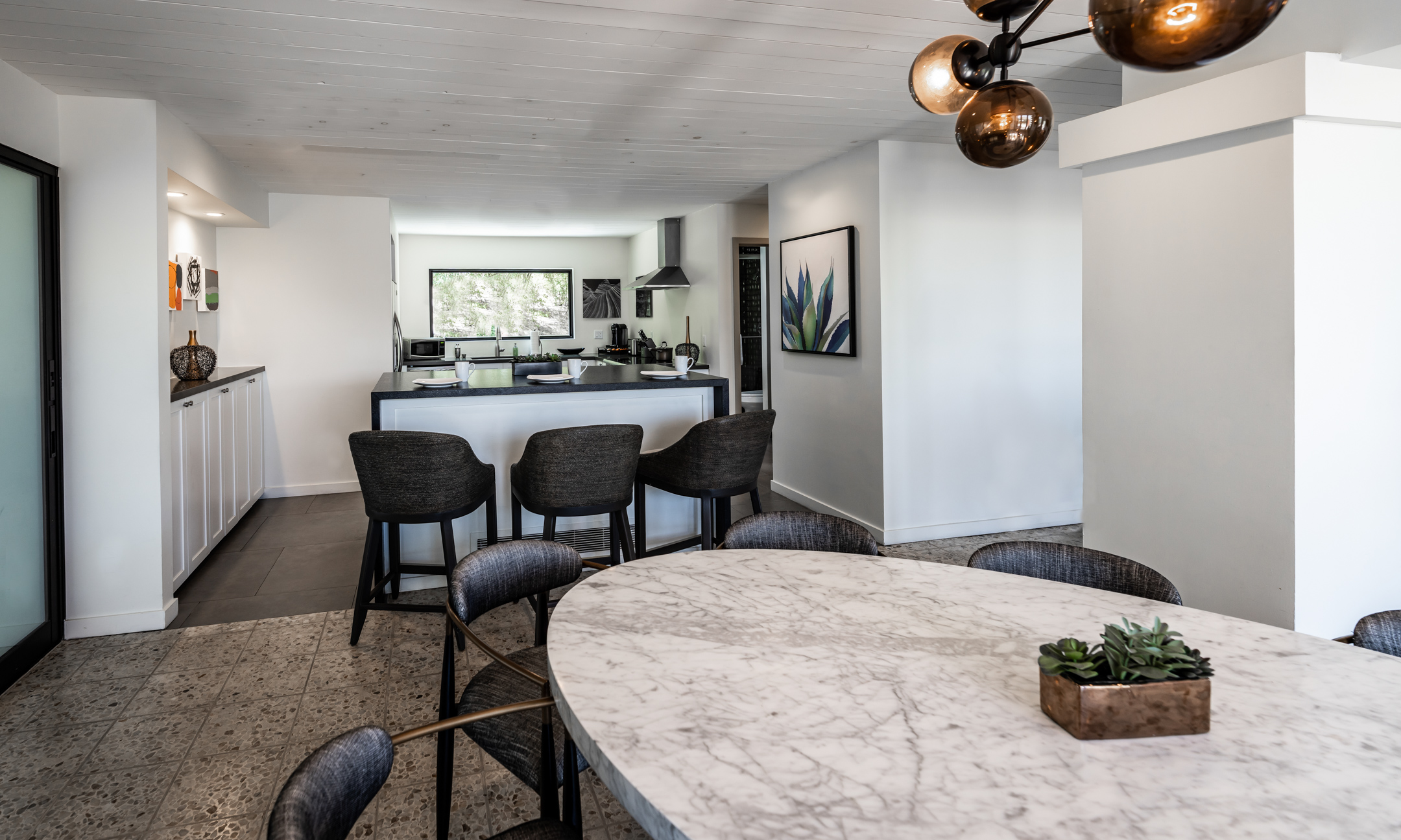 View from entrance of dining room with marble dining table and black chairs, full kitchen with island and chairs.