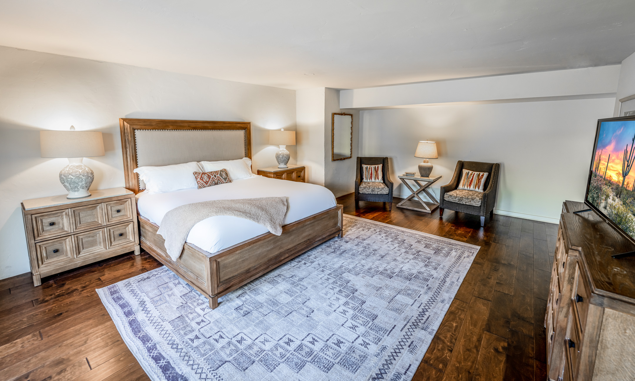 Master bedroom with King bed, blue carpet, wood flooring, two dressers, seating area and flatscreen television.