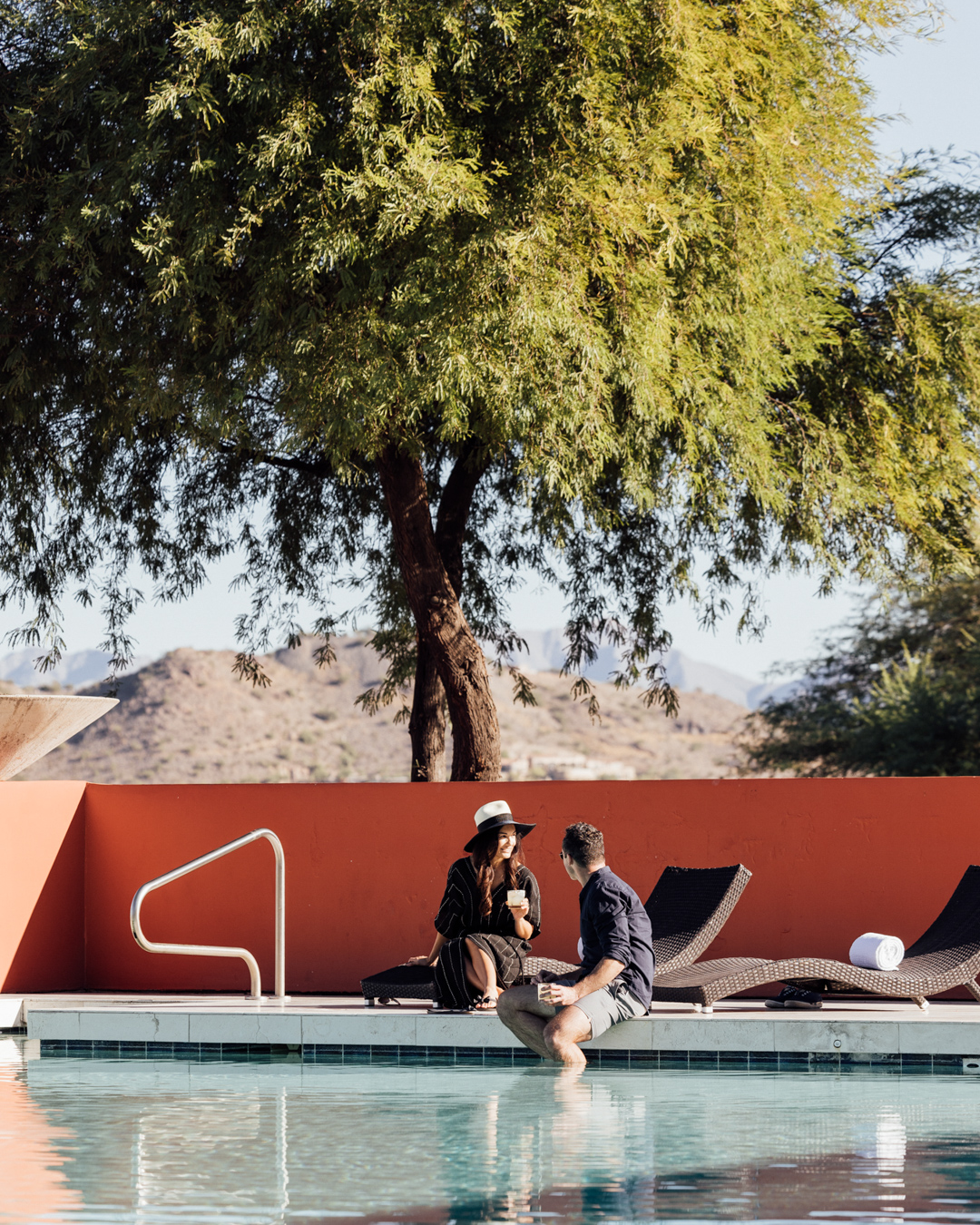 Couple lounging with drinks poolside and feet dangling in Infinity Pool