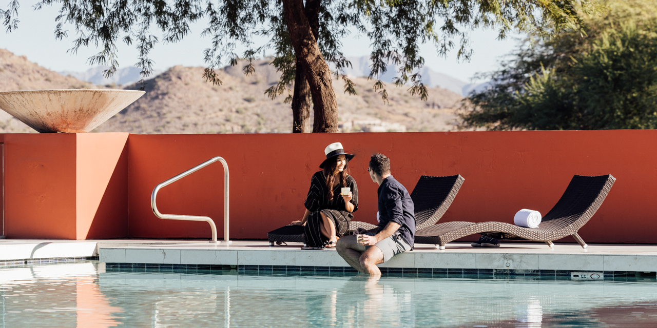 Couple lounging with drinks poolside and feet dangling in Infinity Pool