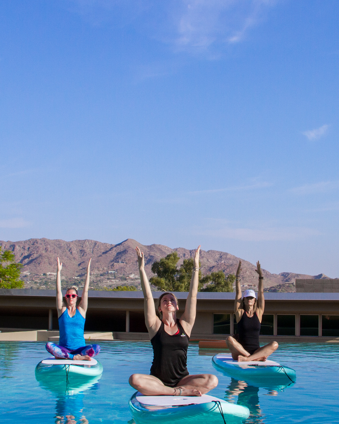 A group of women sitting on paddle boards in Sanctuary's Infinity Pool doing yoga skyward yoga pose