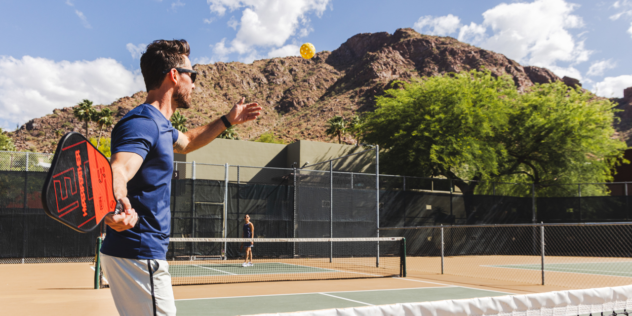 Couple playing Pickleball on Sanctuary's outdoor court with Camelback Mountain in background.