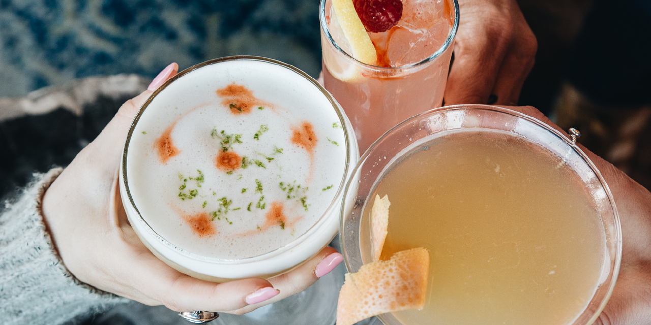 Three hands holding brightly colored cocktails in a cheers