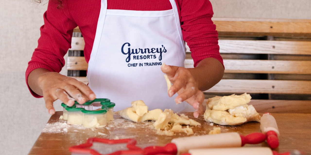 A child in a Gurney's Resorts apron shapes cookies out of dough