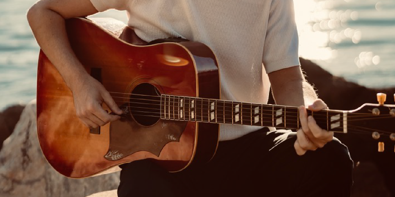 A closeup of a man holding a guitar with water in the background