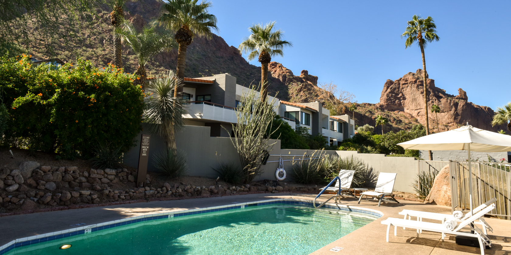 Sanctuary's Eastern Satellite Pool with lounge chairs and umbrellas, surrounded by lush desert landscape and mountain views.