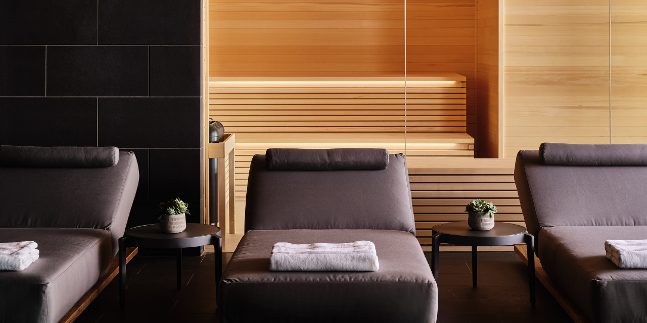 Three gray lounge chairs lined up with the sauna in the background at the Seawater Spa BathHouse