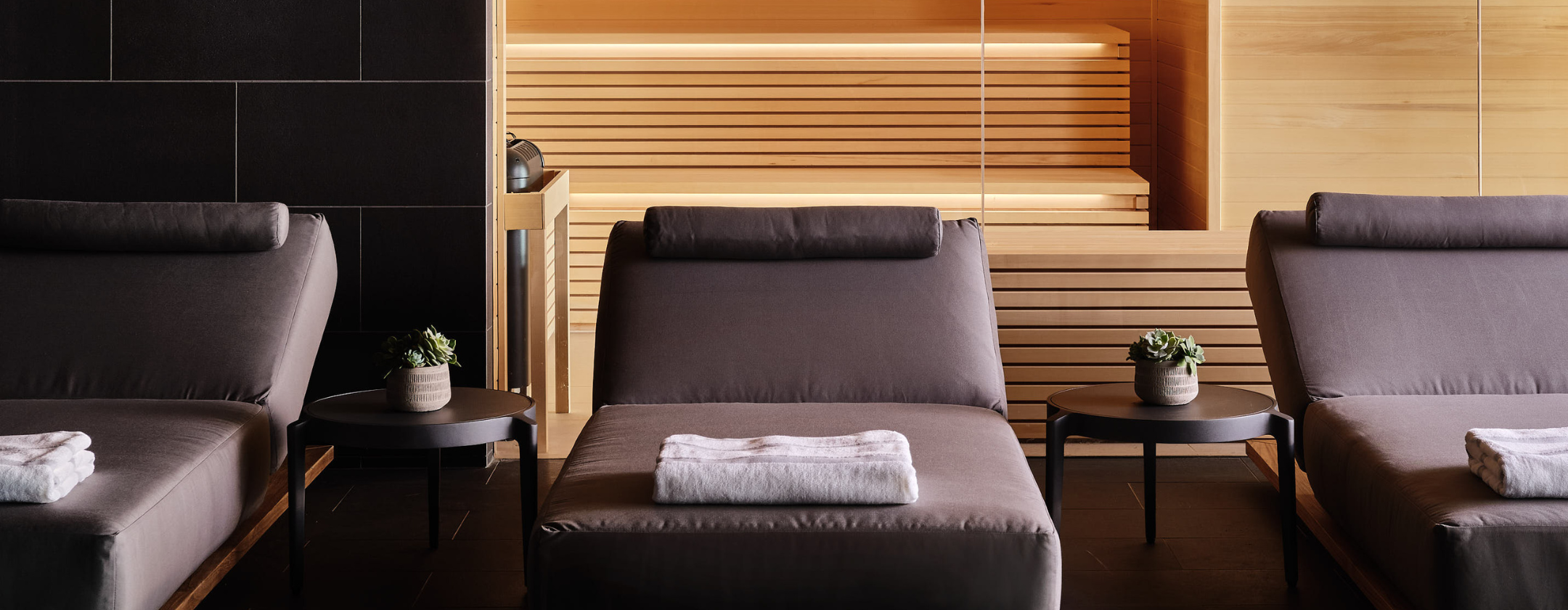 Three gray lounge chairs lined up with the sauna in the background at the Seawater Spa BathHouse