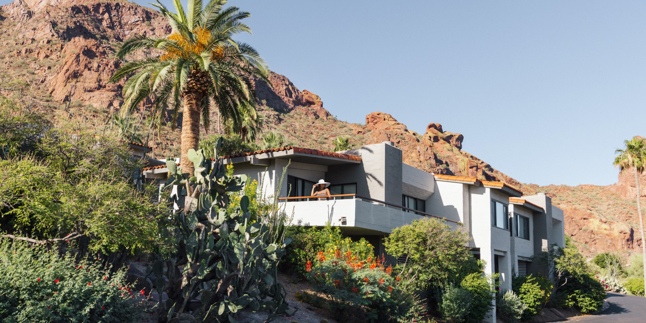 Woman standing on balcony with glass of wine enjoying spectacular desert mountain surroundings.