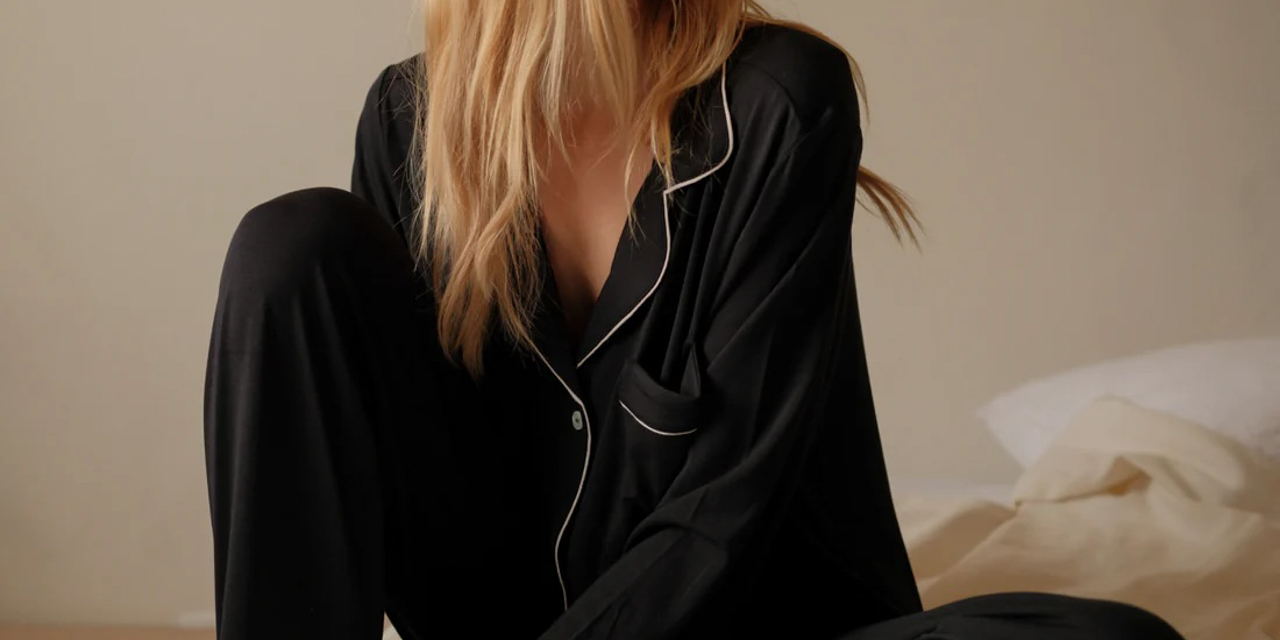 Woman lounging in comfortable black Eberjey Pajamas with white lining.