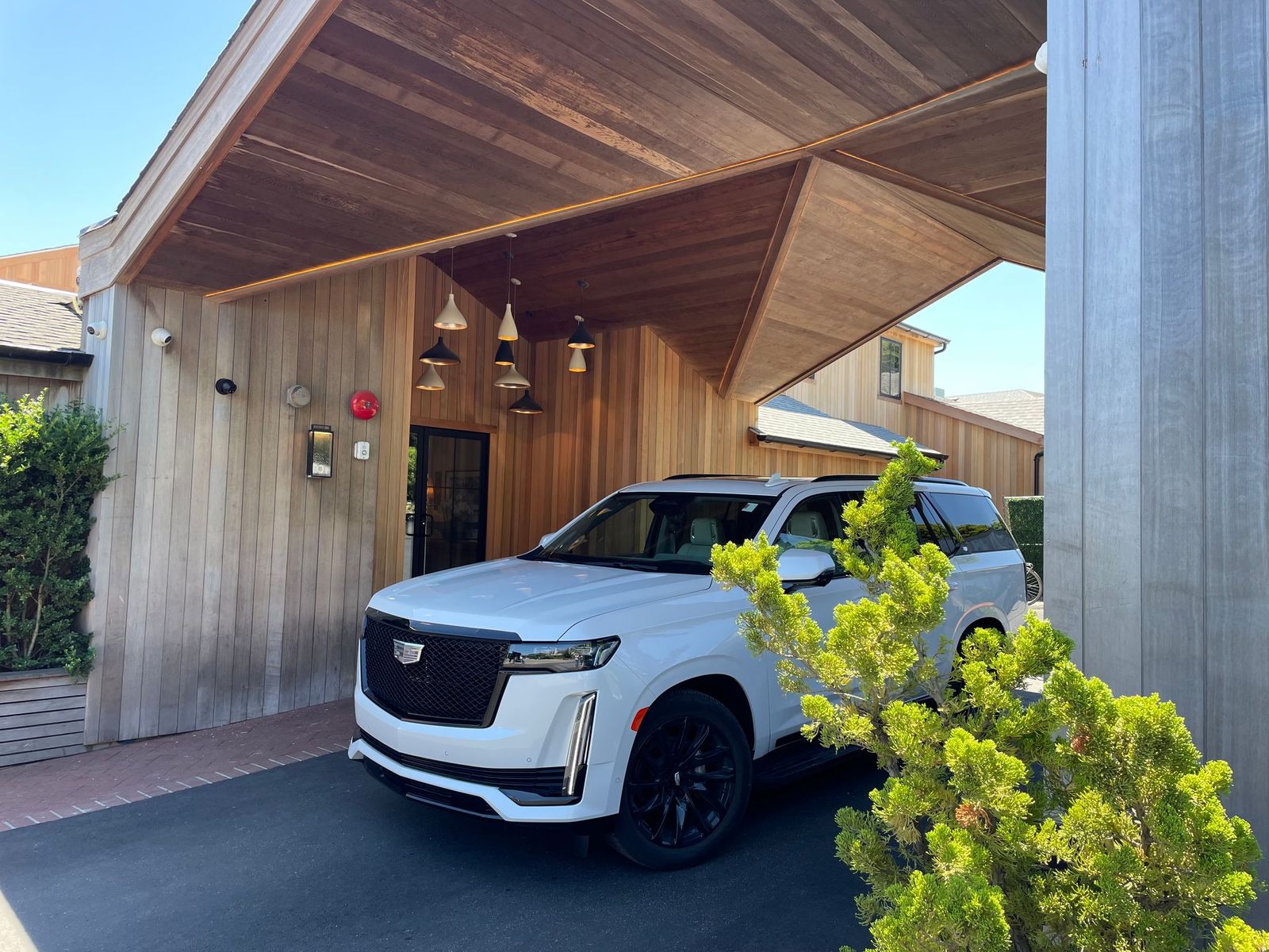 A white SUV parked under a wooden carport at a building with wood siding.