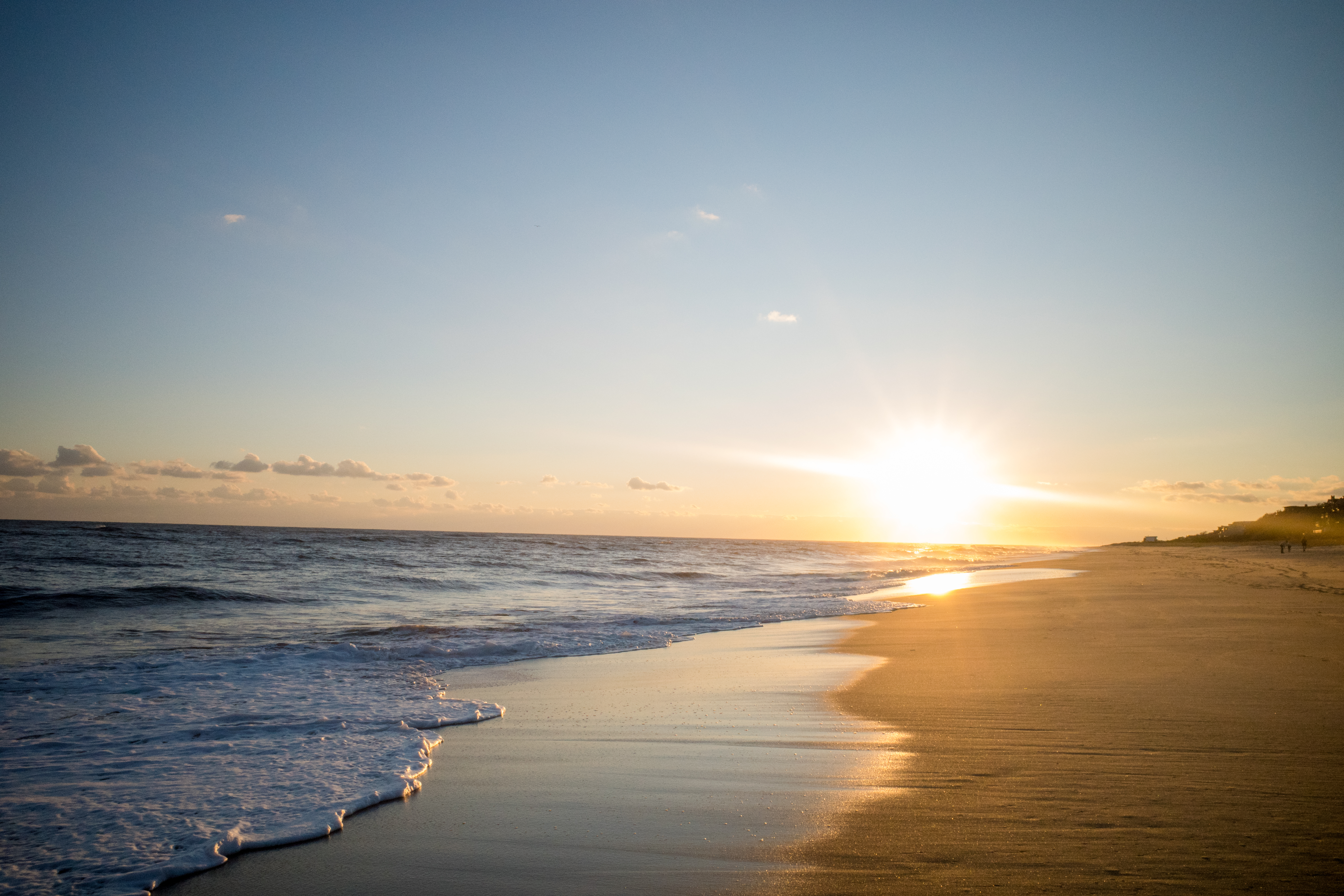 Sun setting over a tranquil beach, casting a golden glow on the sand and sea, with gentle waves lapping the shore.