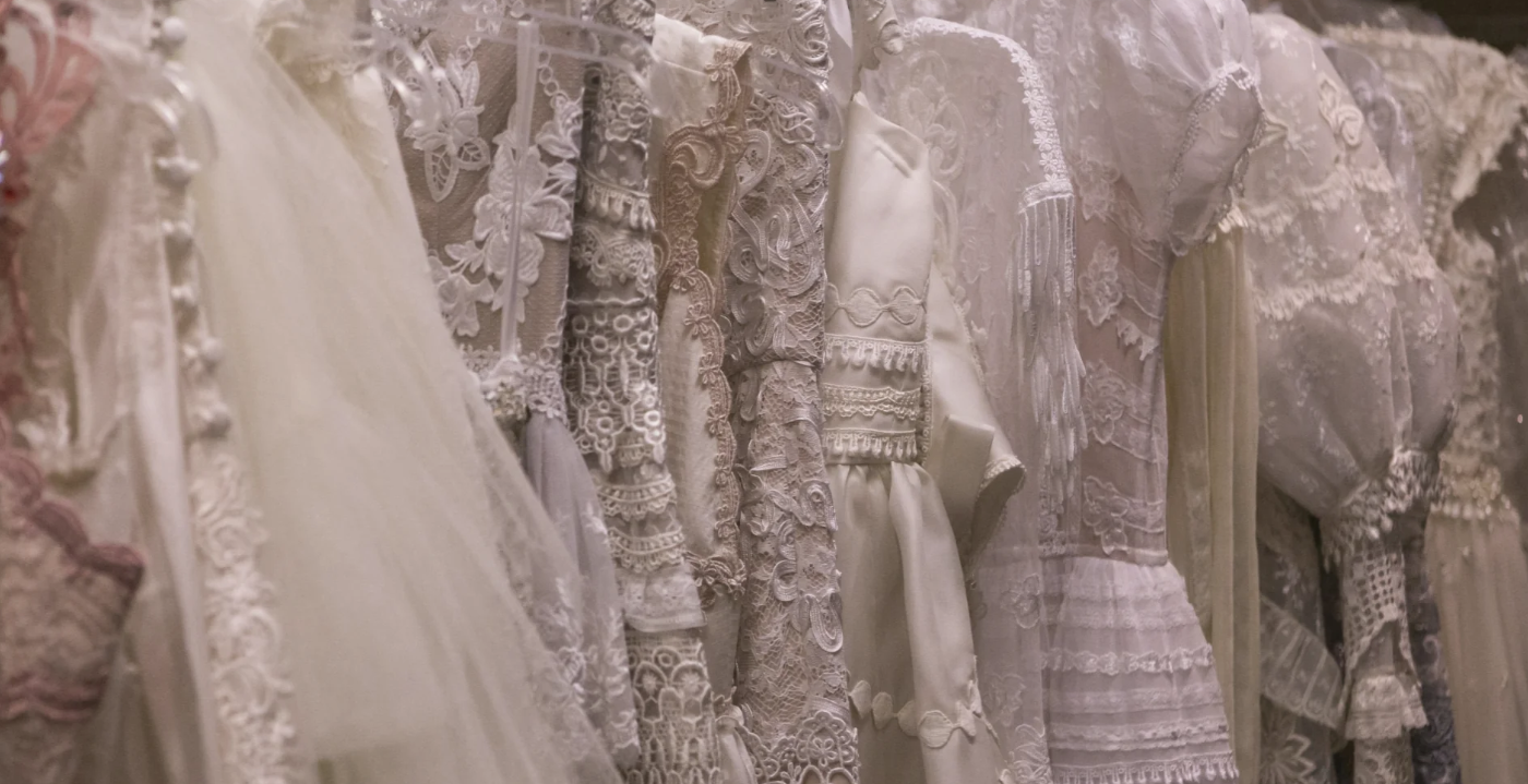 Elegant white lace and satin dresses hanging in a row, showcasing intricate patterns and textures.