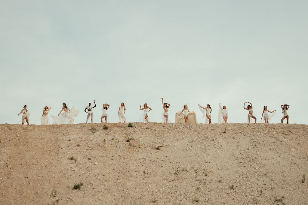 People in light clothing standing on top of a sandy ridge against a pale blue sky.